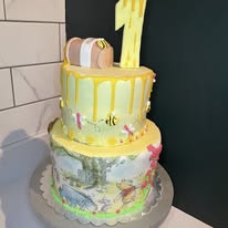 Two-tier first birthday cake with a yellow drip, hand-painted woodland scene and gold number one