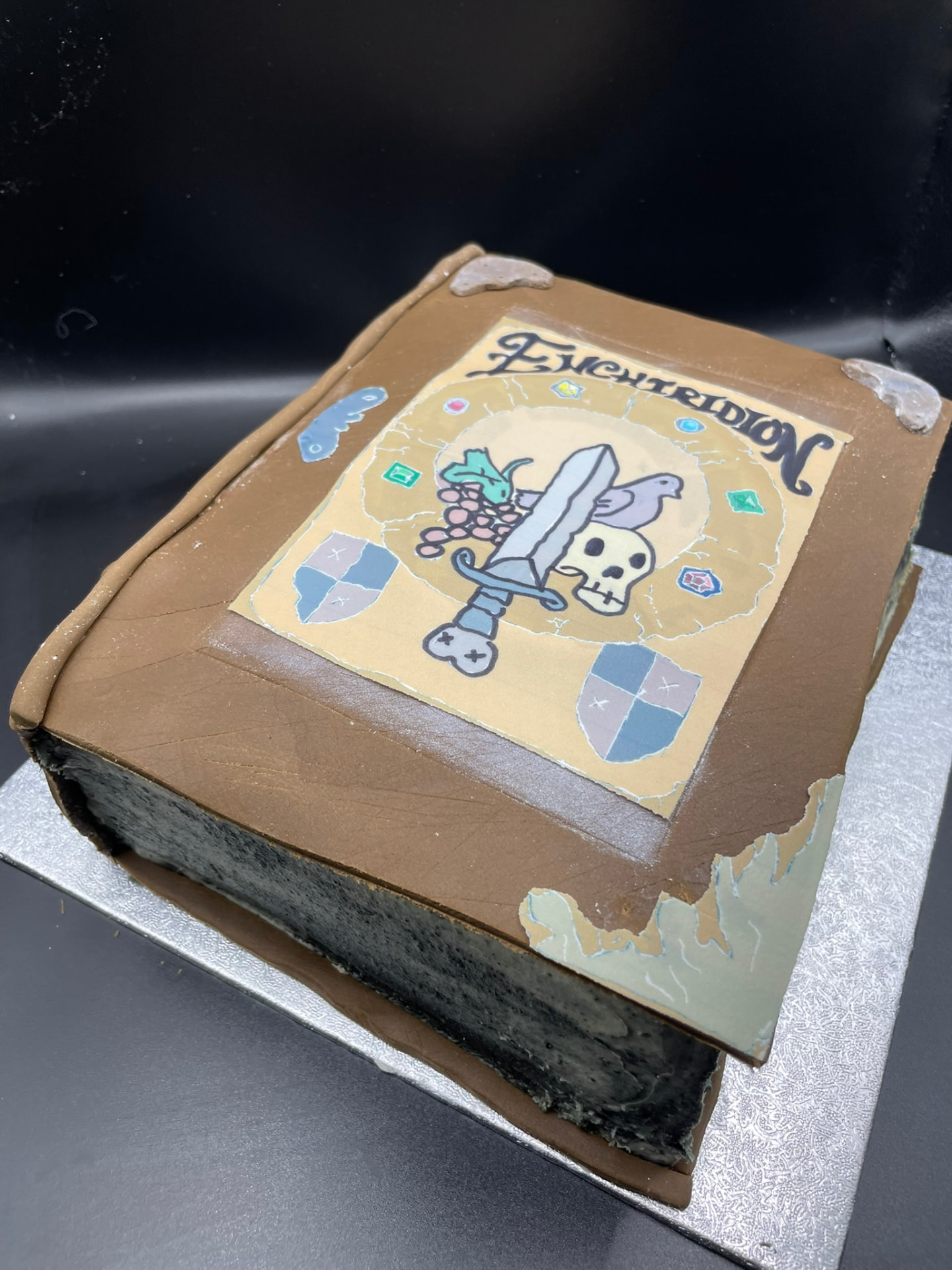 Sculpted cake shaped like an aged leather spell book with a hand-painted cover