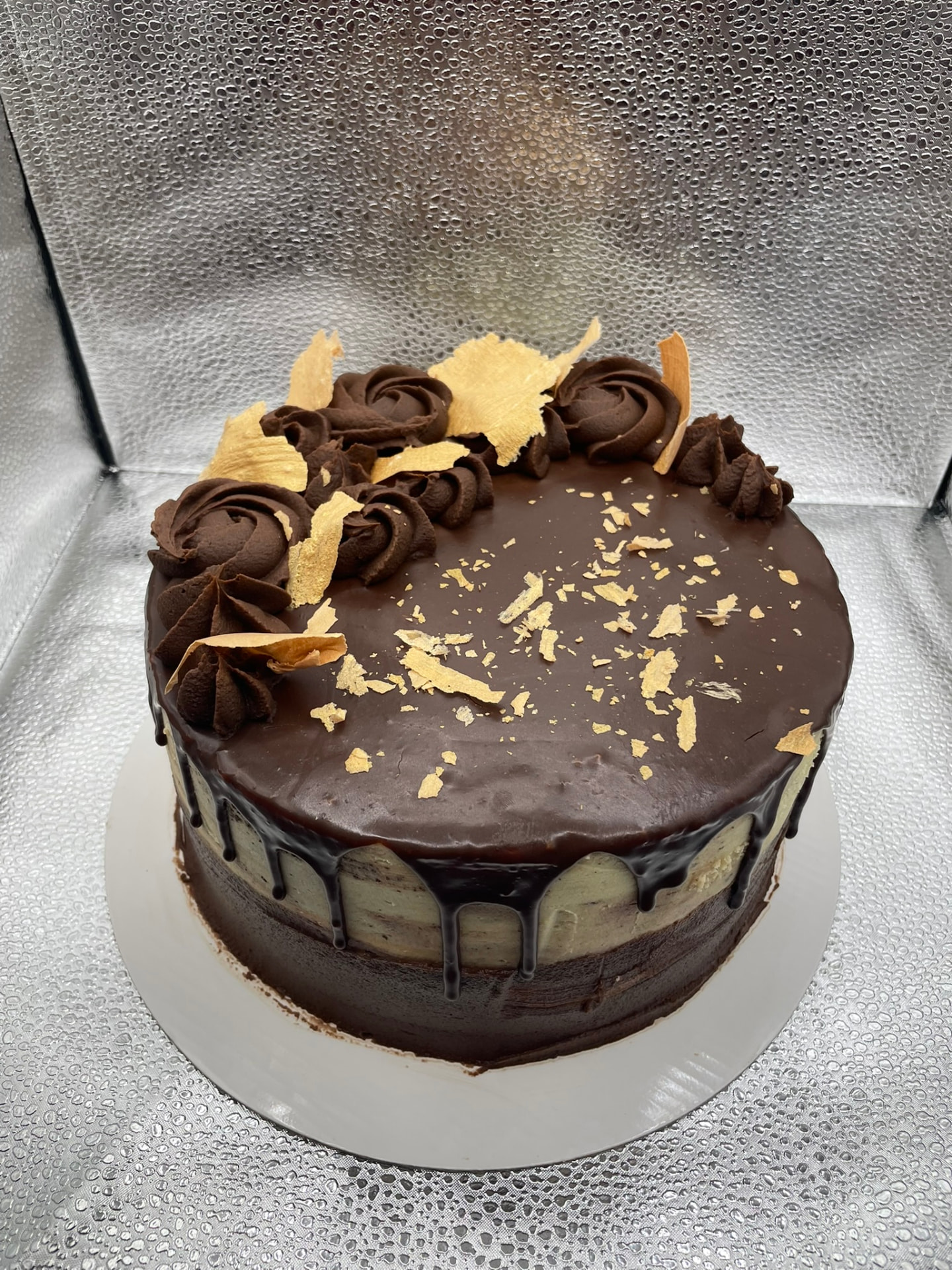 Chocolate ganache drip cake topped with piped rosettes and gold shards