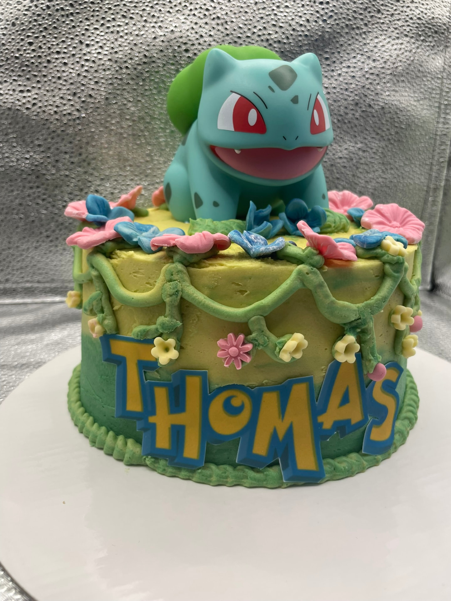 Green and yellow character cake with fondant flowers, vines and a name plaque